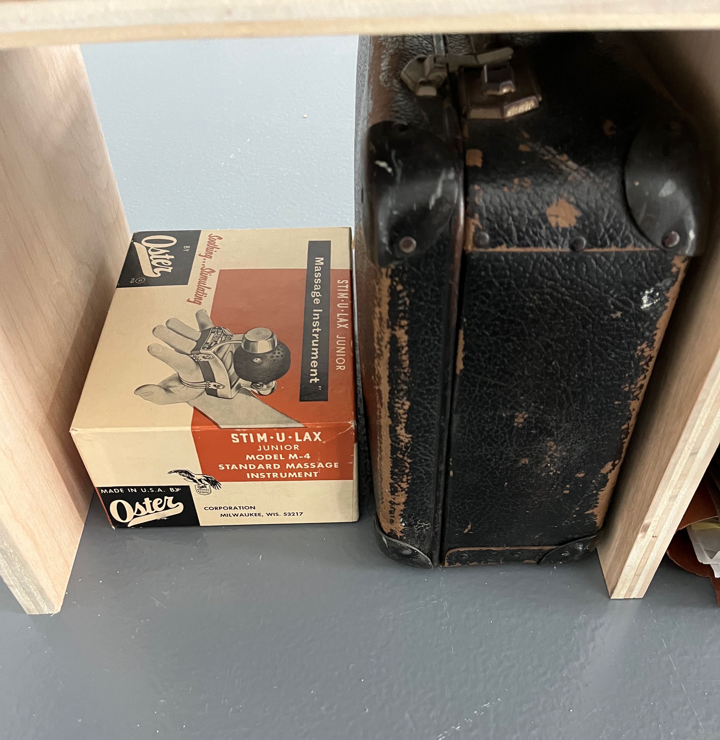 Image of an Oster Stim-U-Lax massager box next to a leather travel case