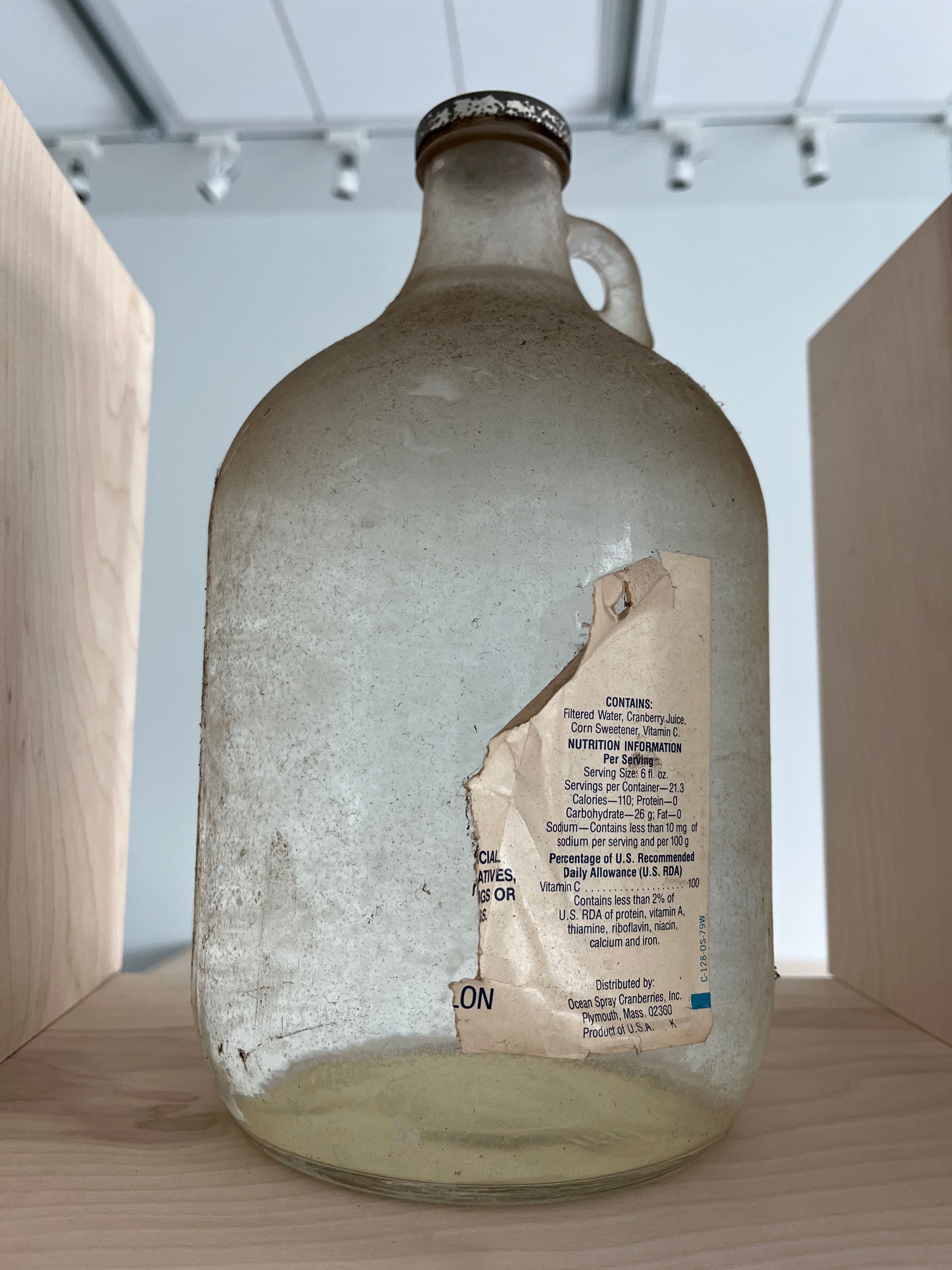 Image of a large glass jug full of clear liquid with a torn label