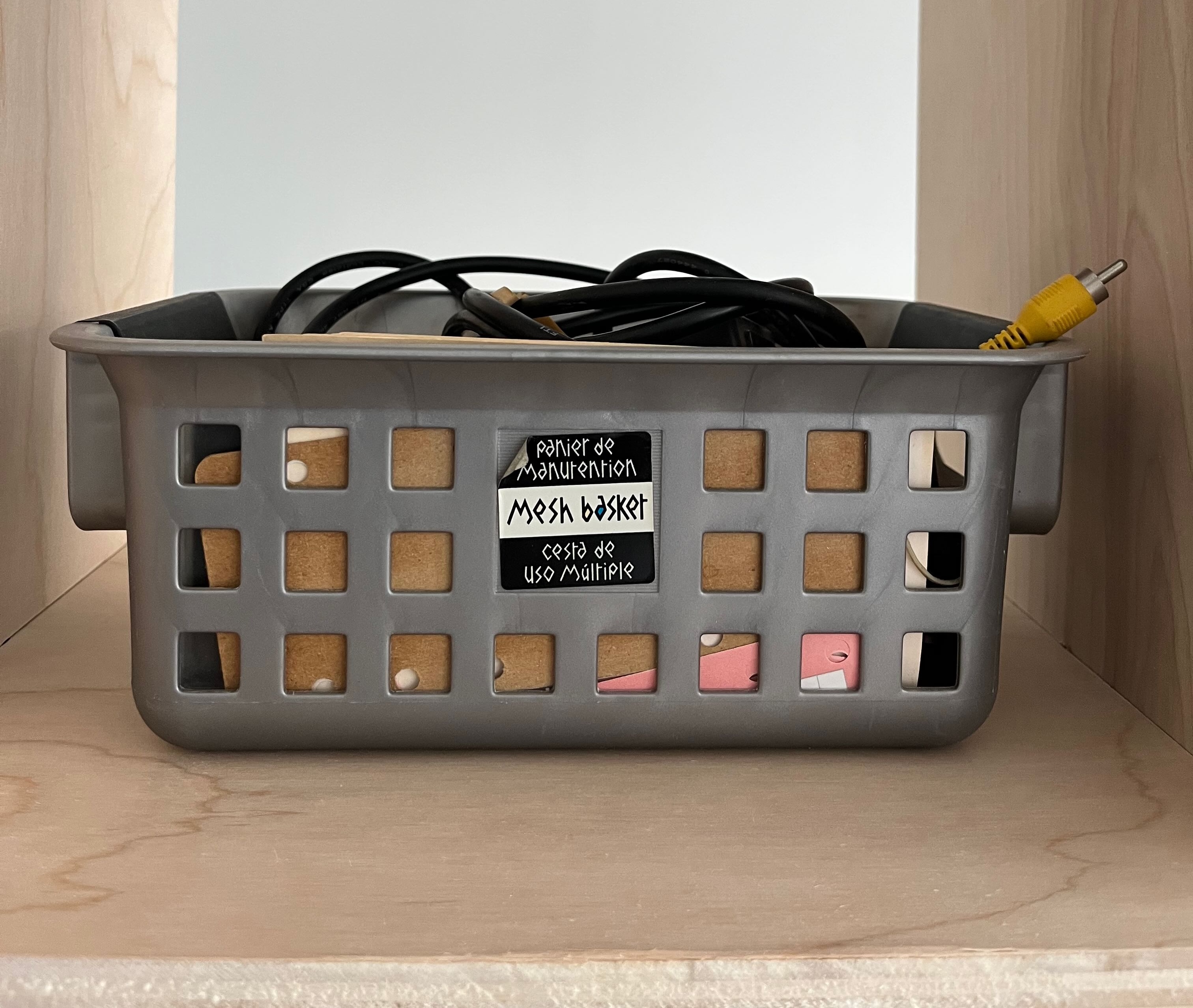 Image of a mesh basket with a label on it that says 'mesh basket' in tree languages. The basket is filled with junk including papers, cables, and synthetic feathers