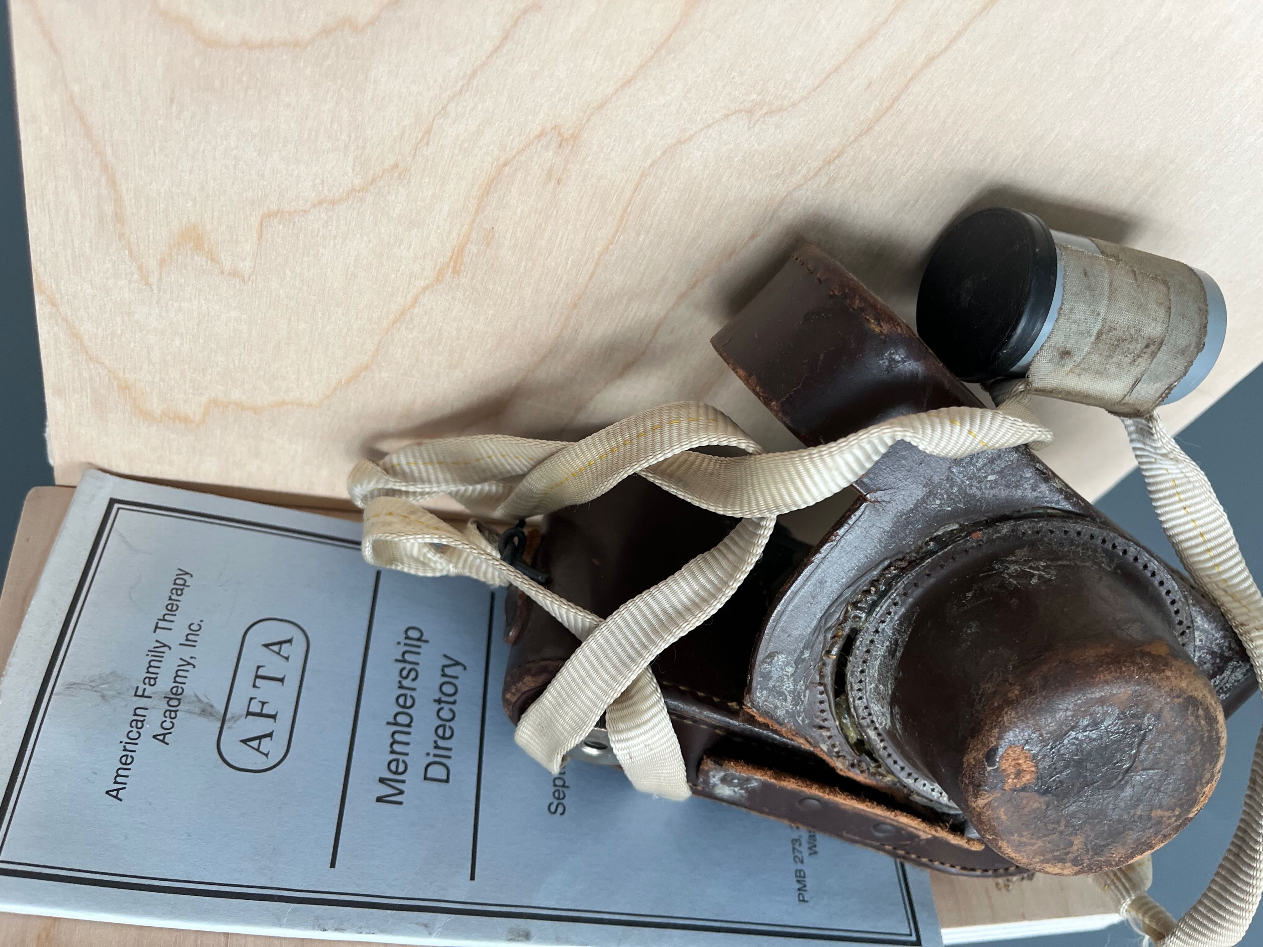 Image of an old camera in a leather case with a film canister stuck to it sitting on top of a Membership Directory flyer from the American Family Therapy Academy